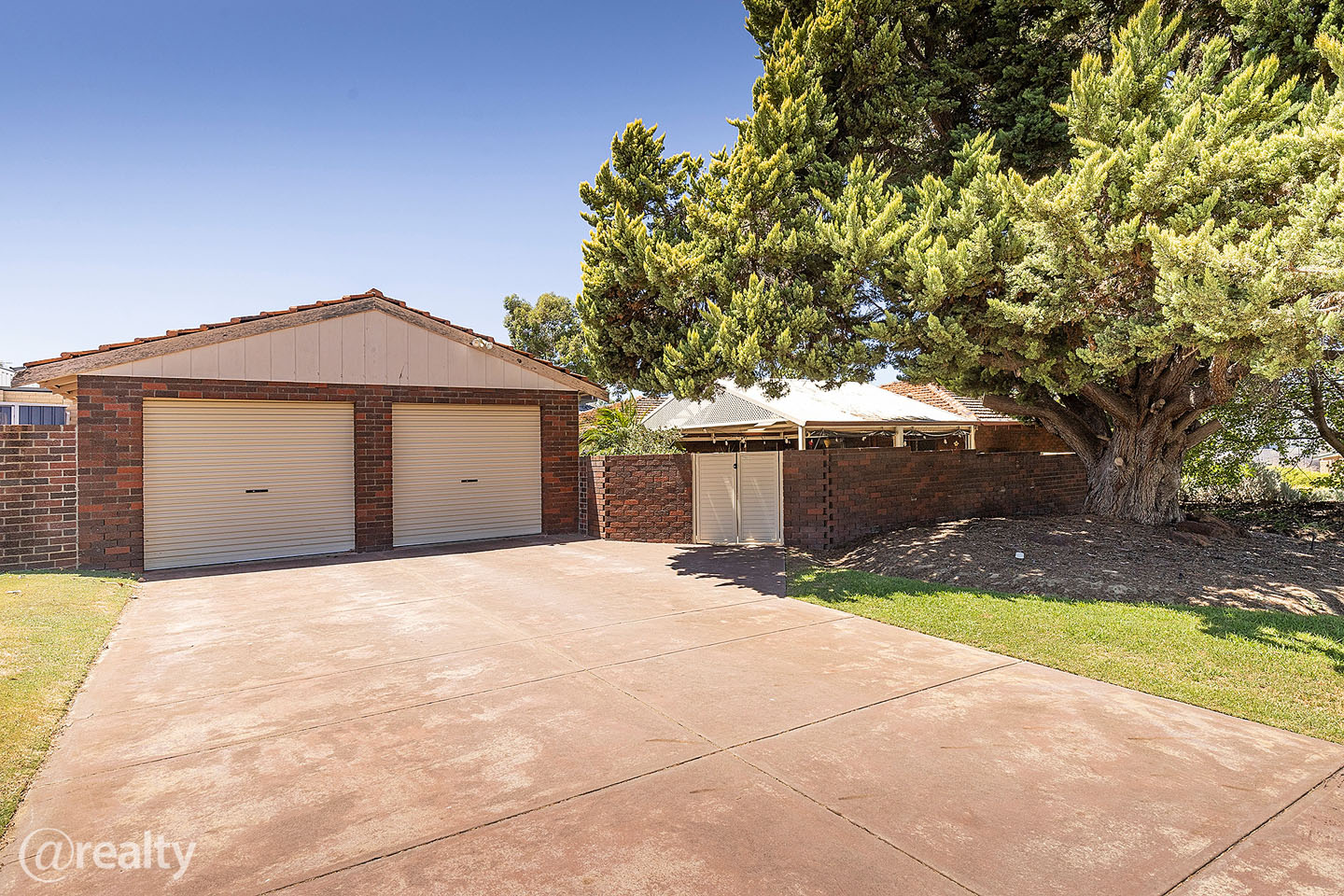 Spacious driveway with double garage and large tree.